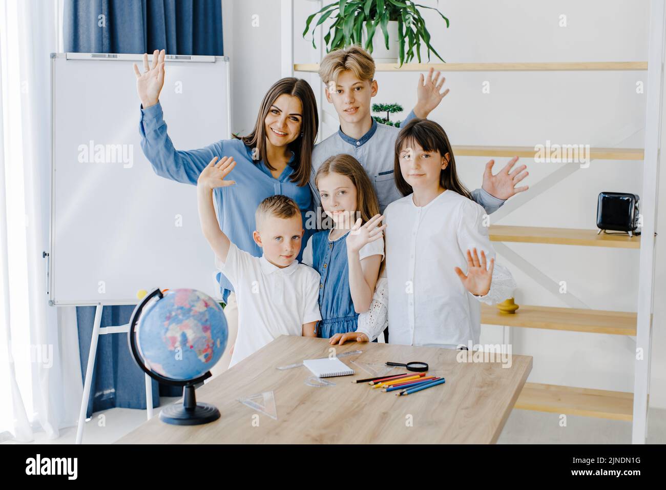 A teacher and schoolchildren of different ages stand in a spacious classroom and smile, looking into the camera. Learning concept Stock Photo