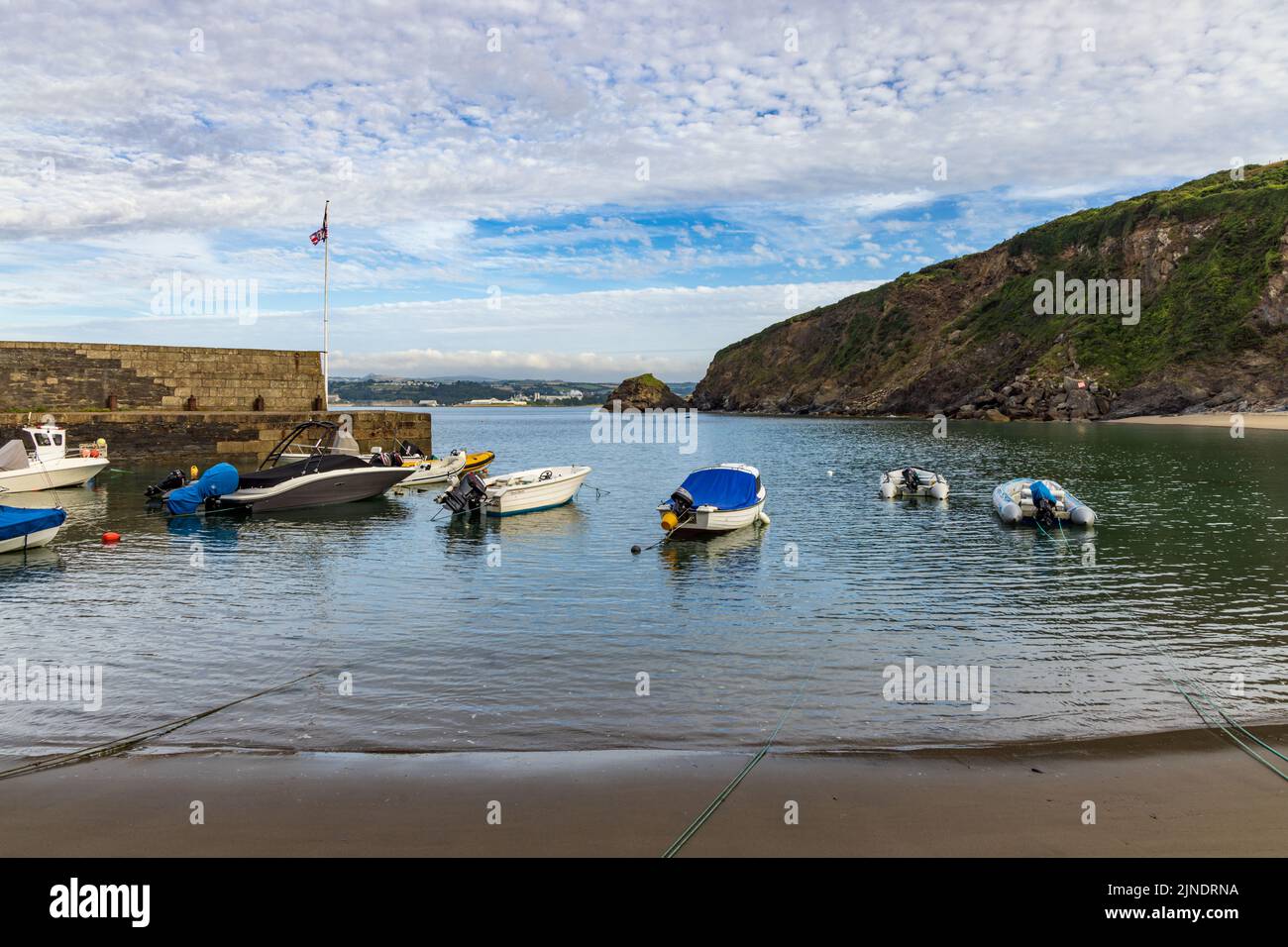 Pleasure boats berthed at Polkerris in Cornwall, a delightful sandy cove with a small harbour. Killyvarder Rock can be seen in the distance. Stock Photo