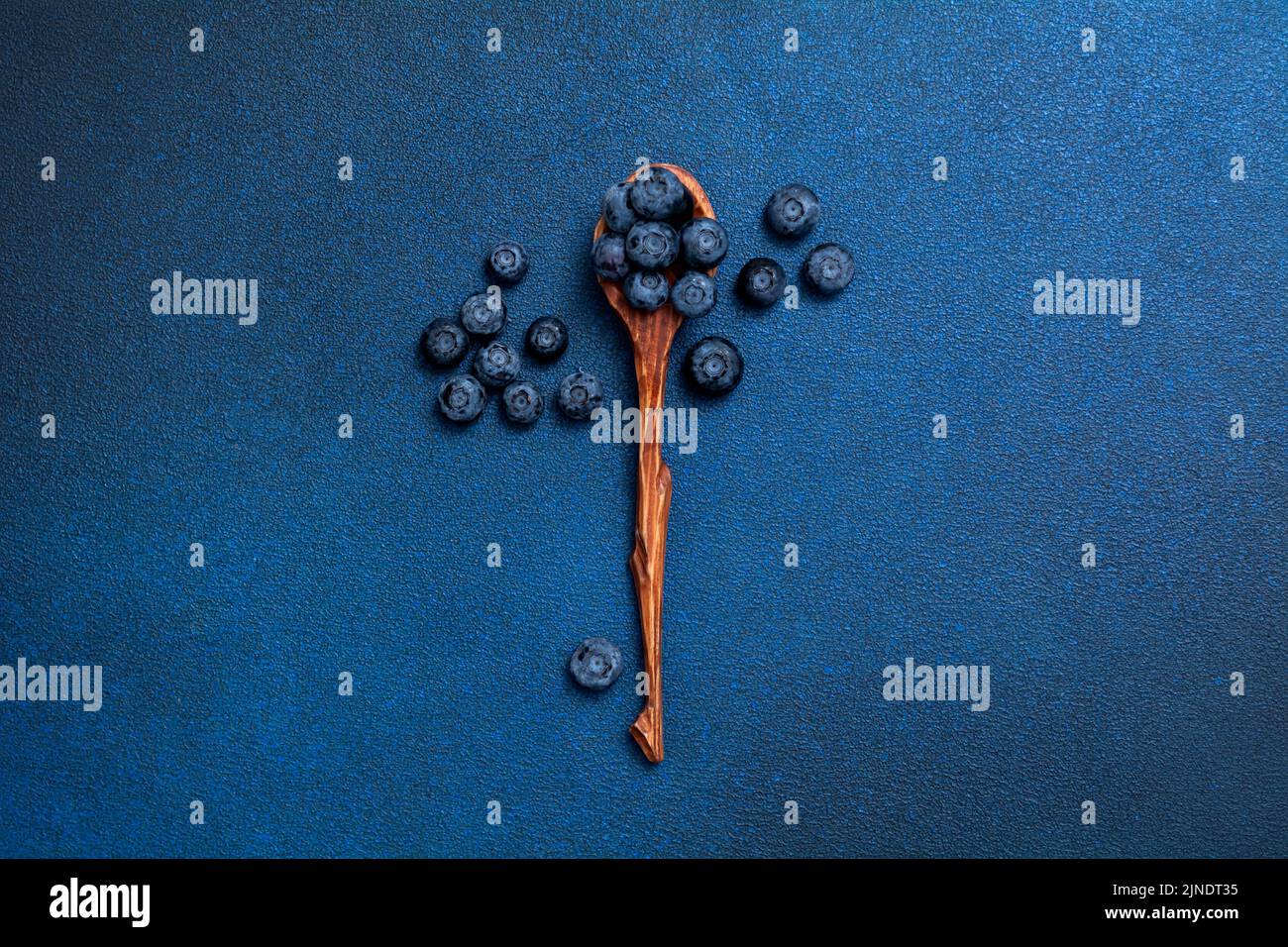Fresh blueberries in a wooden spoon. Berries on a blue background. View from above. Stock Photo
