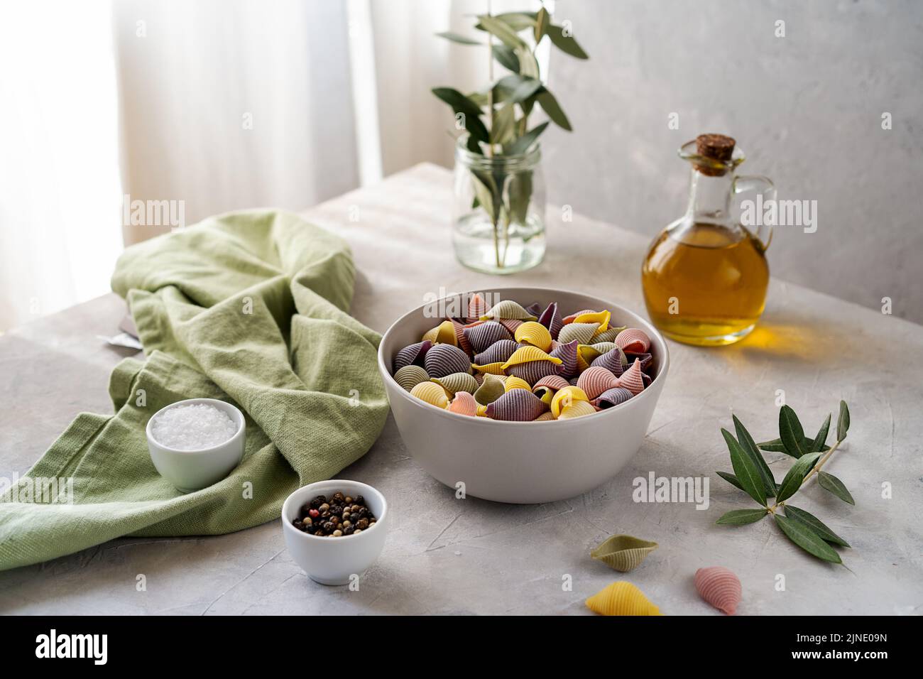 Colorful Italian pasta conchiglie or seashells in bowl, olive oil, salt