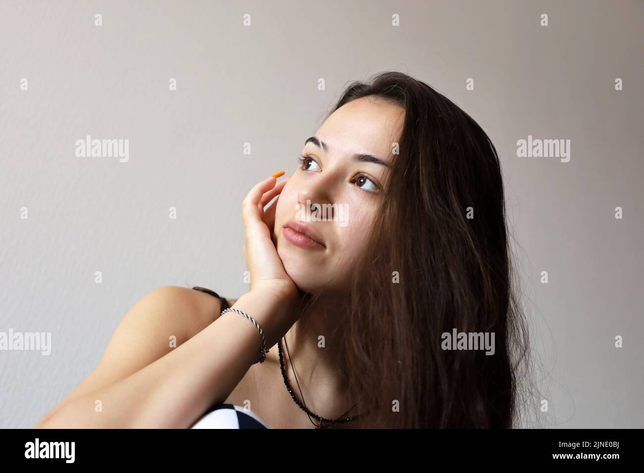 Portrait of attractive teen girl with long hair touching her dreaming face with her hand with orange acrylic nails. Female beauty, skin care Stock Photo