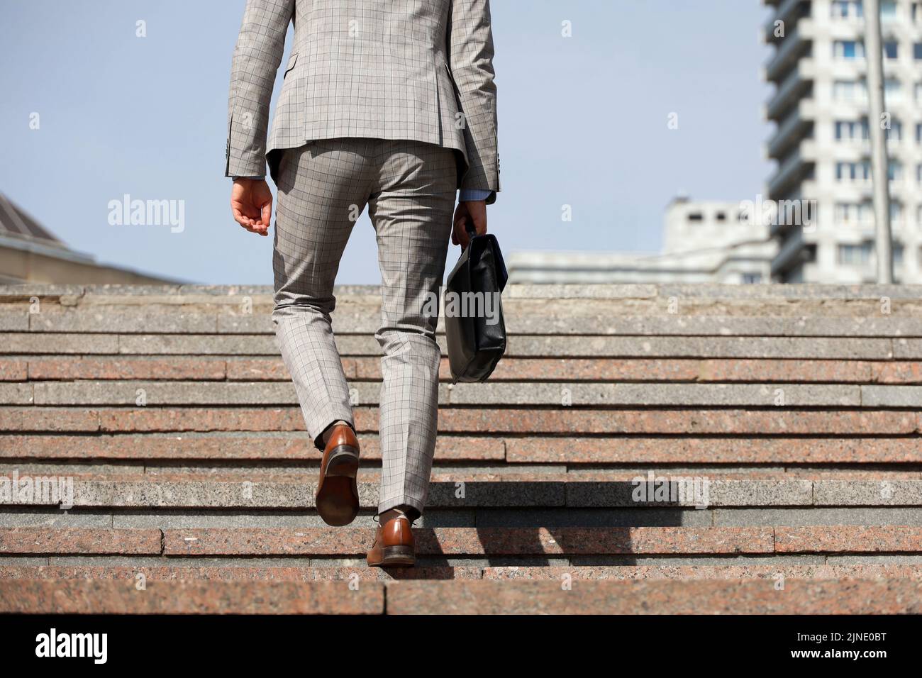 Man in a business suit with leather briefcase climbing stone stairs in city, male legs in motion on the steps. Concept of career, success Stock Photo
