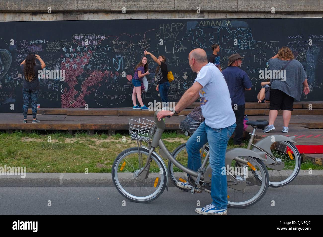 Man on a bicycle stops to join other people by the interactive chalkboard by the Seine river. Beautiful summer day outdoor in Paris, France. Stock Photo