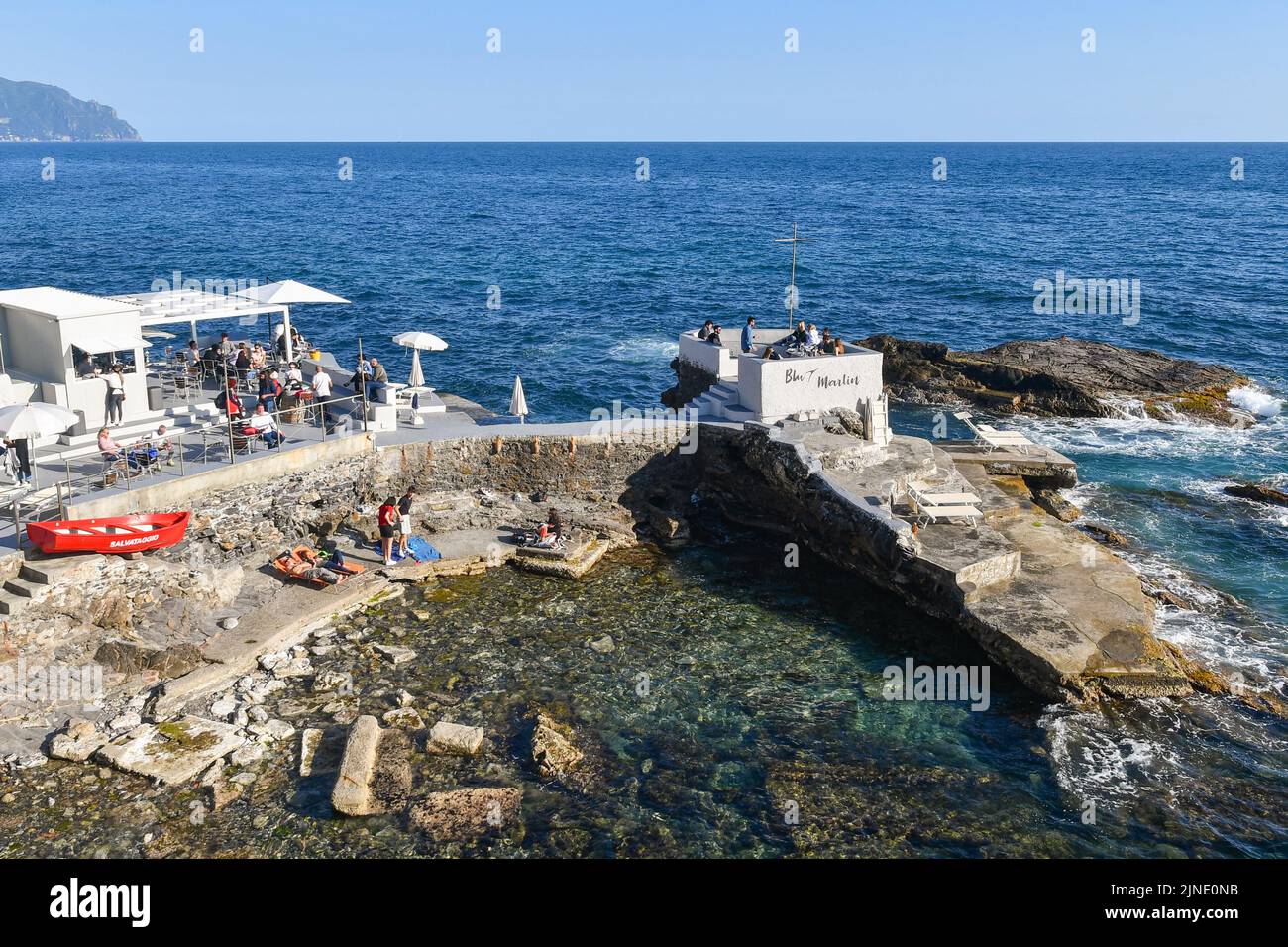 High-angle view of a beach bar on the cliff with people and the promontory of Portofino in the background, Nervi, Genoa, Liguria, Italy Stock Photo