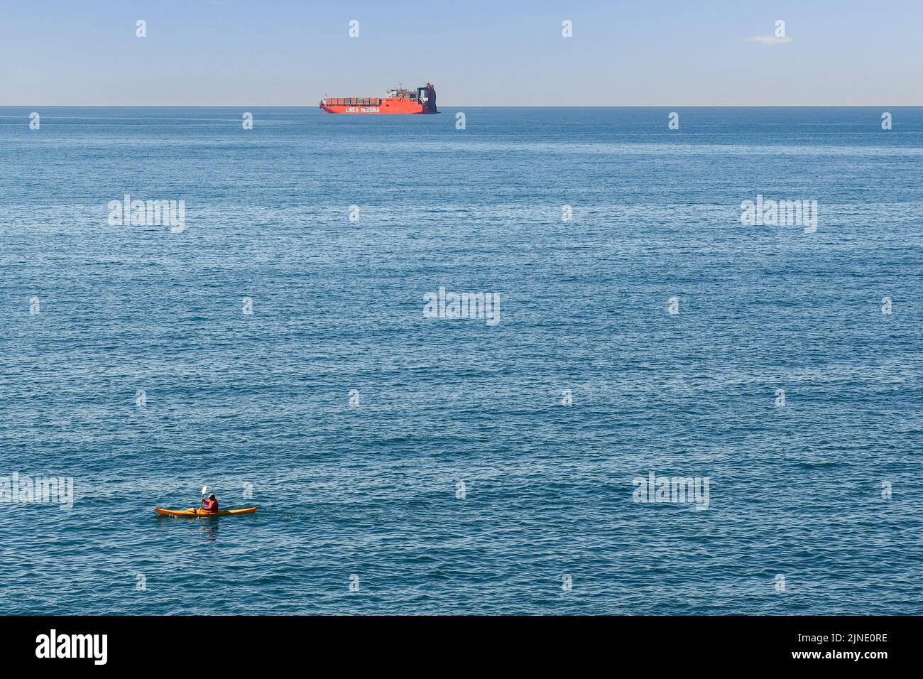 Man kayaking on the shore with a container ship of the Linea Messina, a shipping company based in Genoa, on the sea horizon, Nervi, Genoa, Liguria Stock Photo