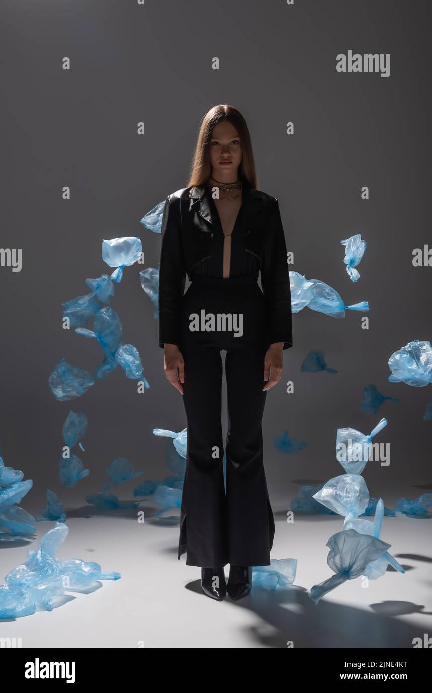 full length of pretty model in black suit posing near blue plastic bags on grey Stock Photo