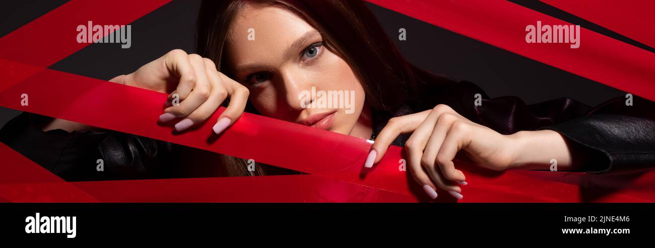 pretty model touching red strips from duct tape isolated on black, banner Stock Photo