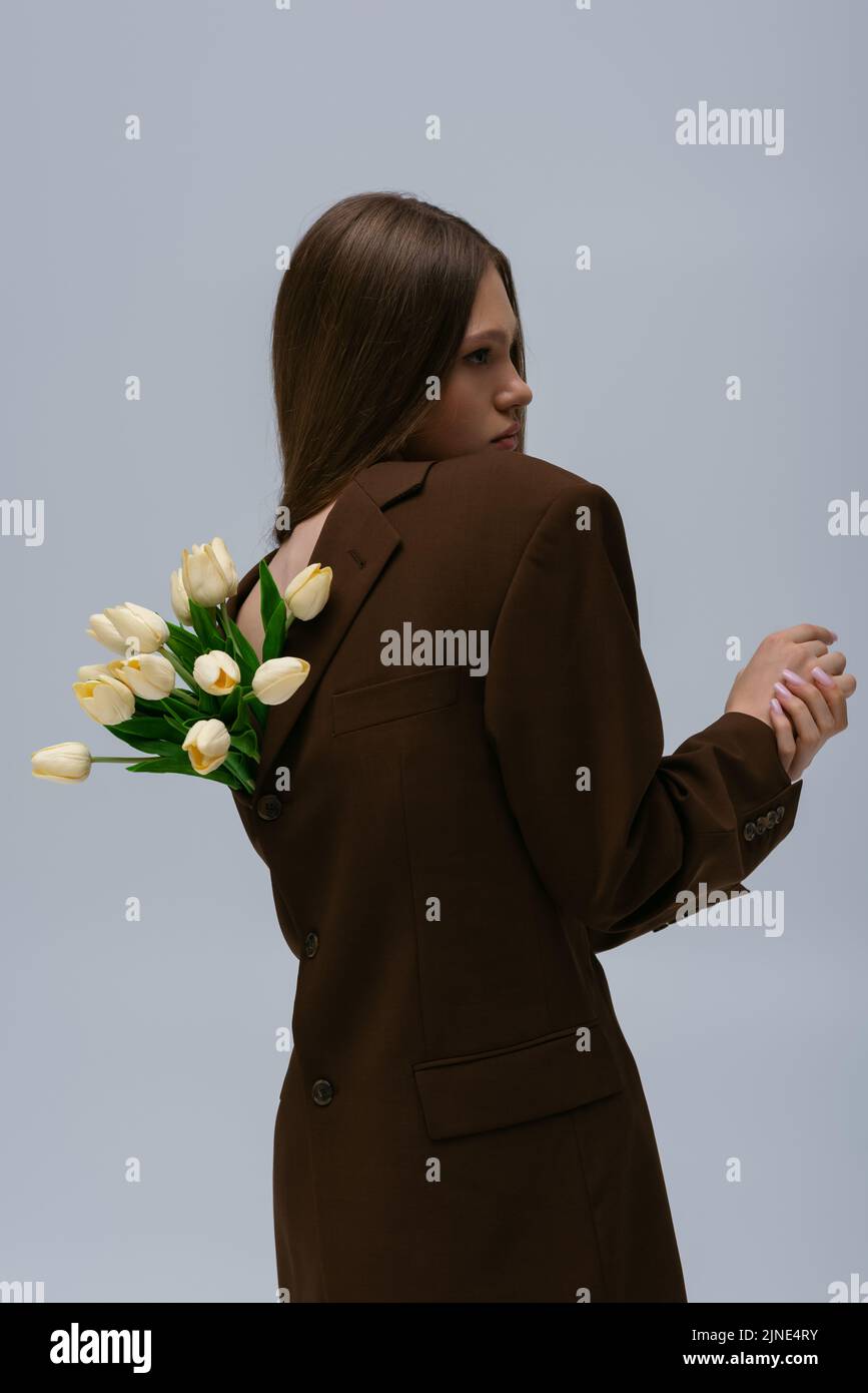 side view of pretty model in brown blazer with tulips posing isolated on grey Stock Photo