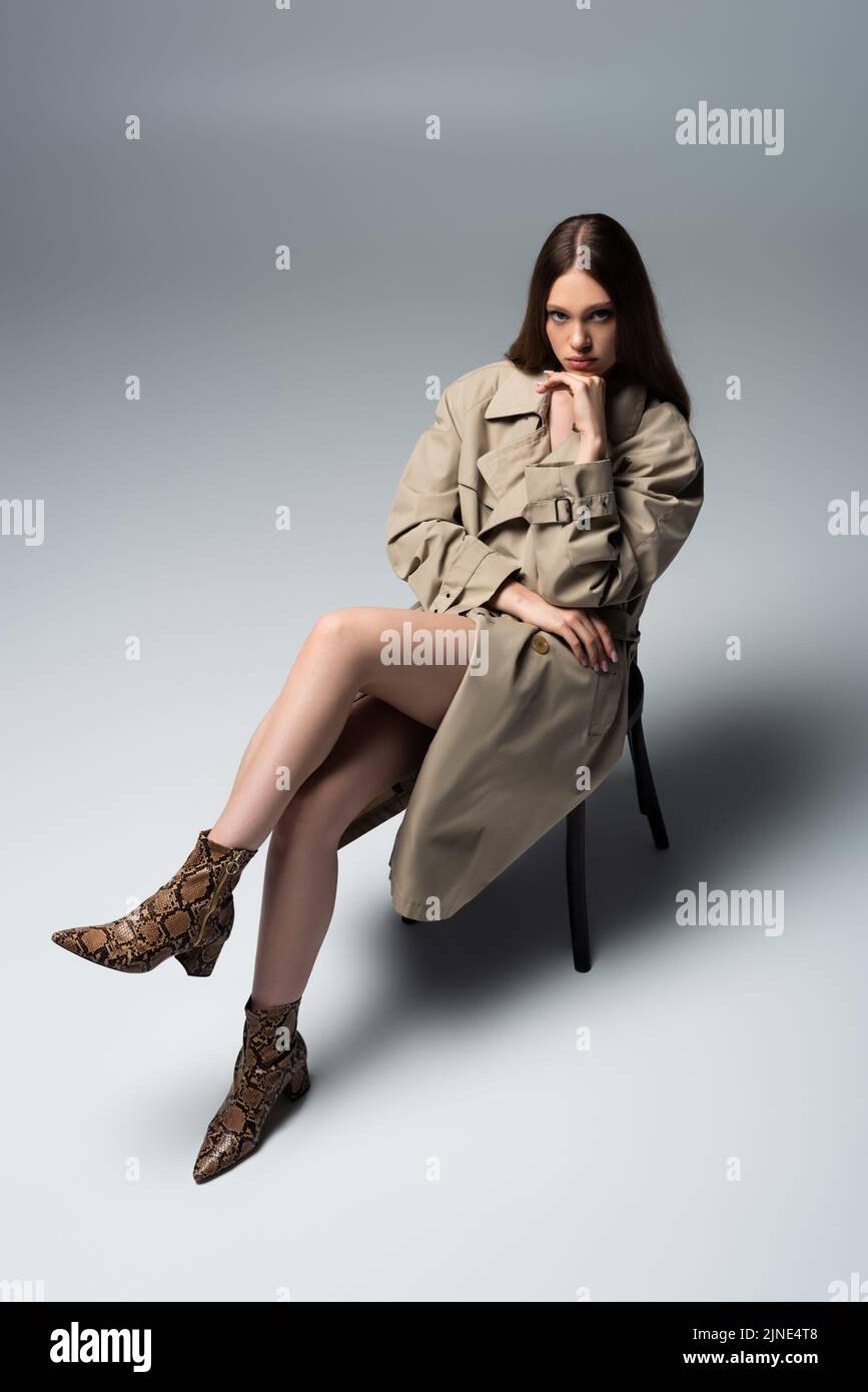 full length of brunette model in autumnal trench coat sitting and ...