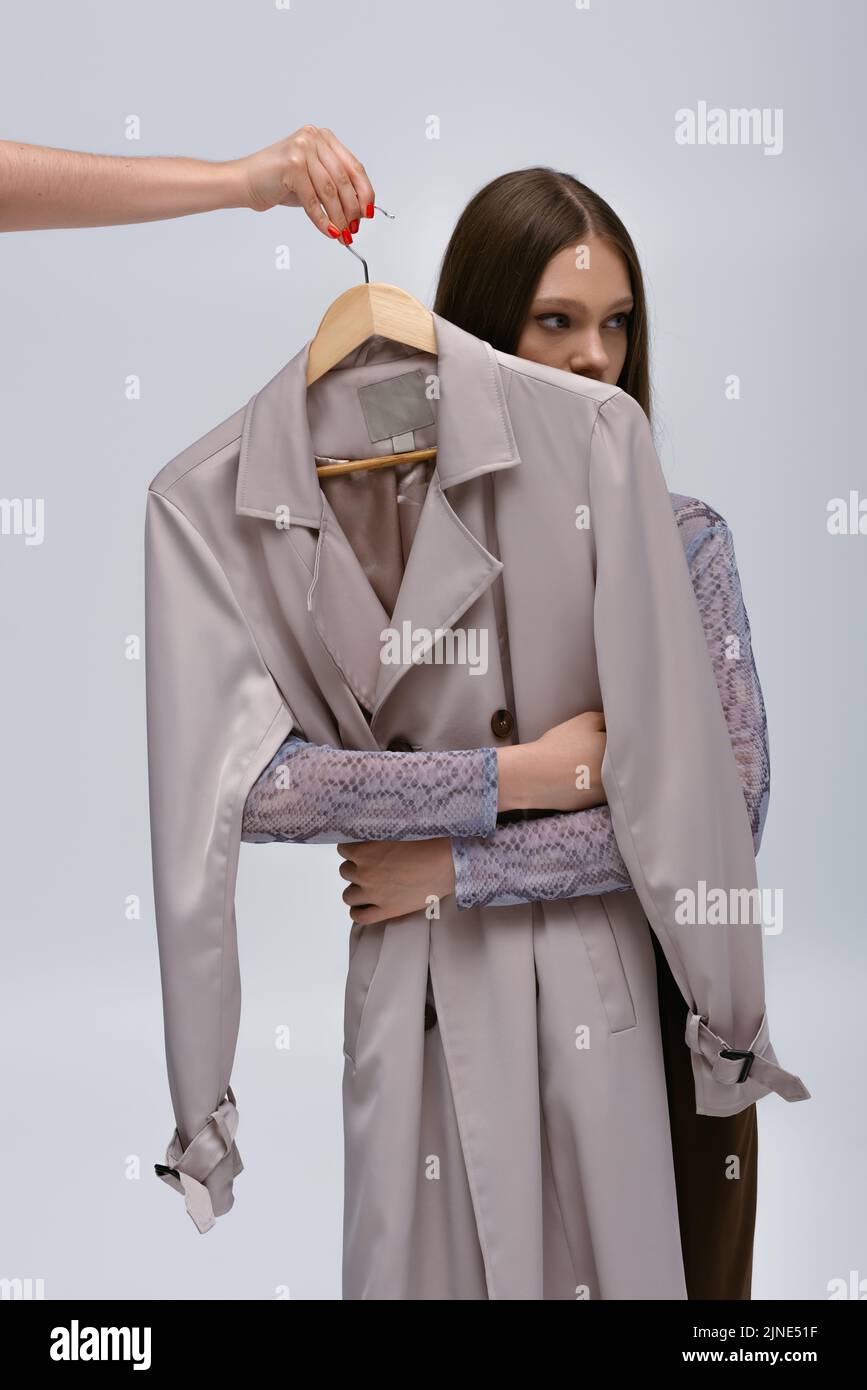 teenage model hugging stylish trench coat while woman holding hanger ...