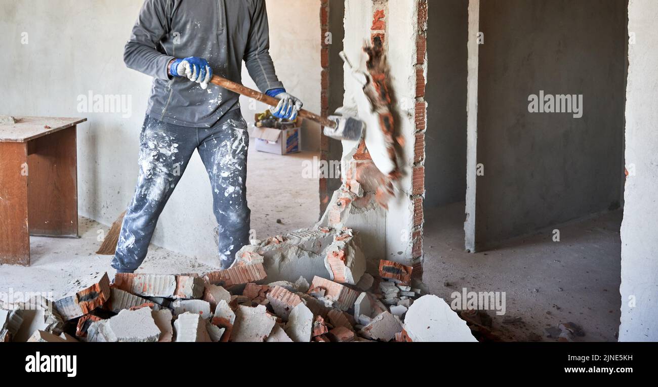 Close up of sledgehammer blow on brick, plaster. Workman striking devastating blow at remnants