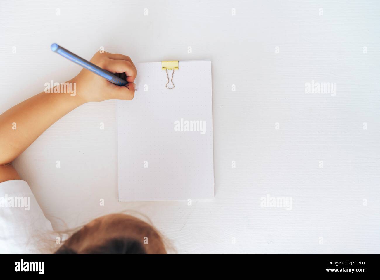 The child writes with a pen on a stack of paper fastened with a ...