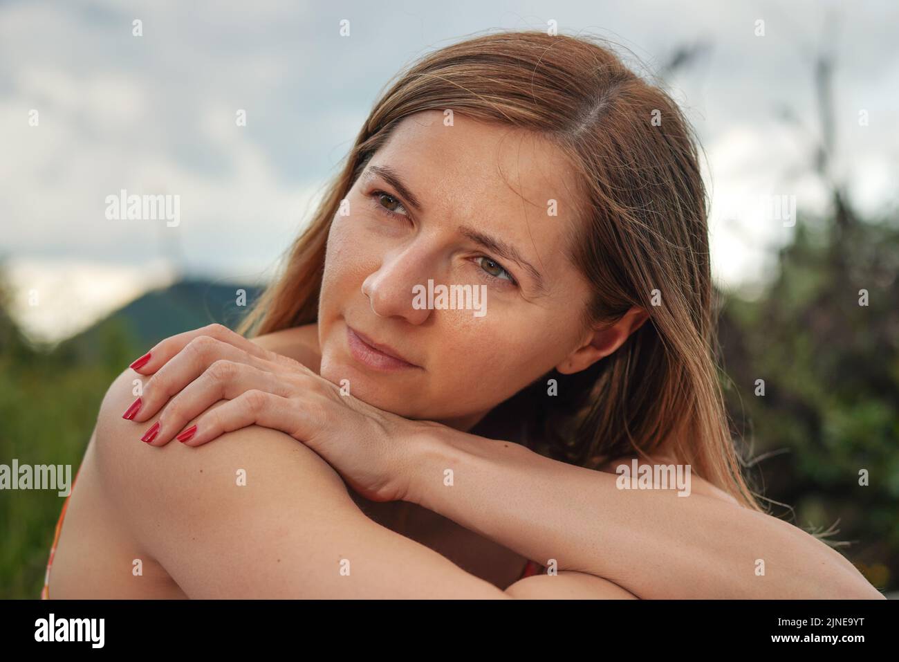 Young woman casual portrait - leaning on her palm and shoulder looking to side, closeup detail, blurred trees background Stock Photo