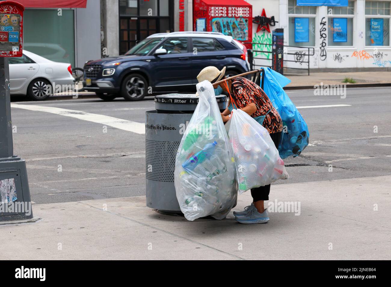 An elderly Asian person reaches into a New York City trash bin for recyclables. Many people, especially elderly Asians, are dependent on the ... Stock Photo