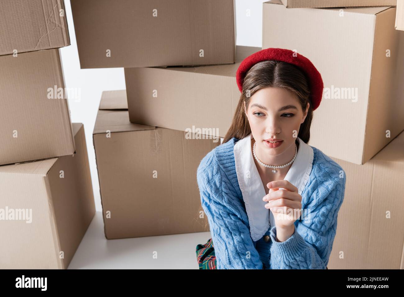 Pretty model in beret looking away near cardboard boxes on white background Stock Photo