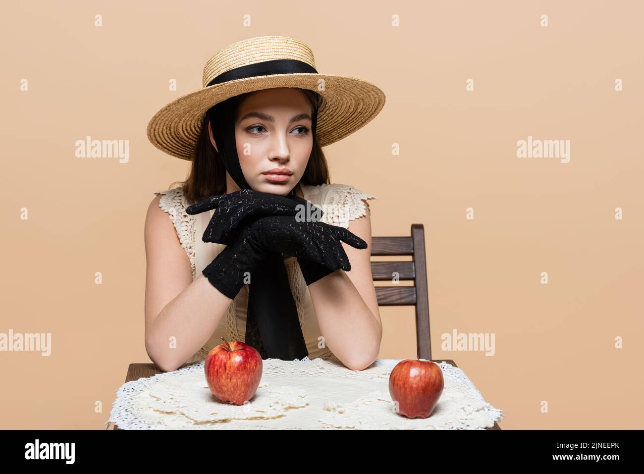 Pretty model in sun hat and gloves looking away near apples isolated on beige Stock Photo