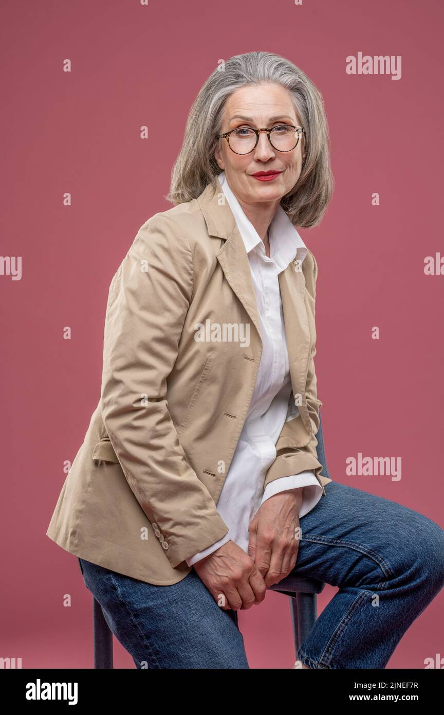 Elegant mature woman in beige jacket sitting on a chair Stock Photo - Alamy