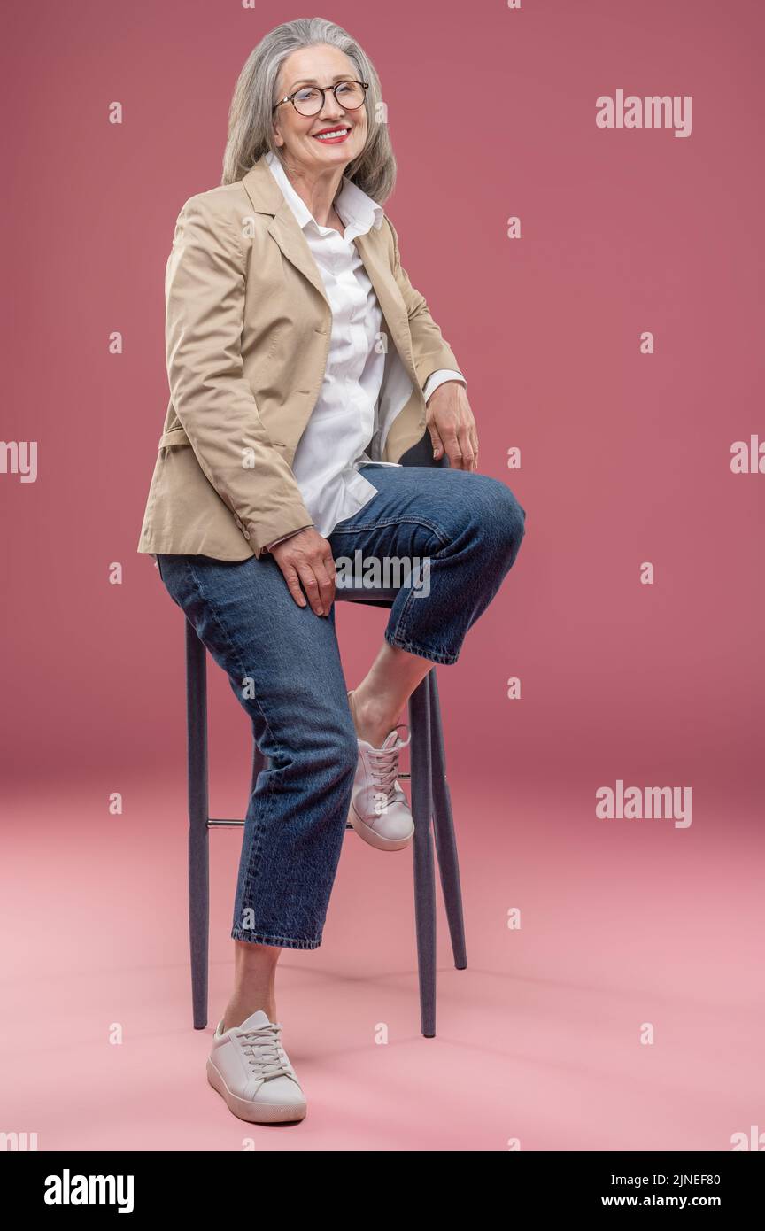 Elegant mature woman in beige jacket sitting on a chair Stock Photo - Alamy
