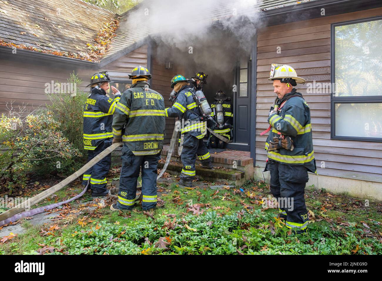 Chief Steve Miller issues commands on his radio as a hose team enters the front door of the building to begin their initial attack as Sag Harbor Fire Stock Photo