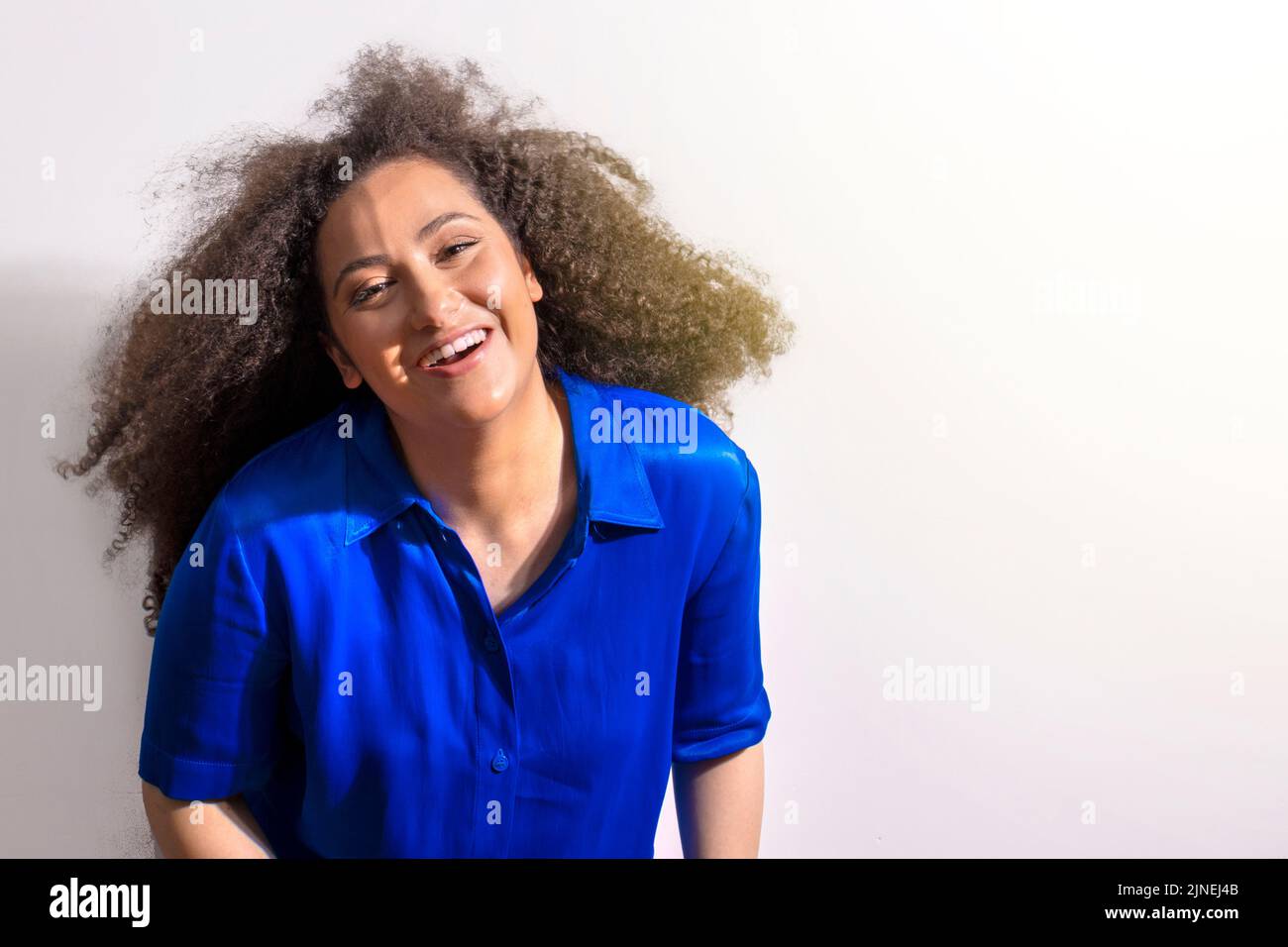 Young girl with afro hair shaking her big hair. Smiling on white background Stock Photo