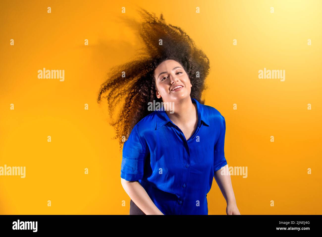 Young girl with afro hair shaking her big hair. Isolated on orange background Stock Photo