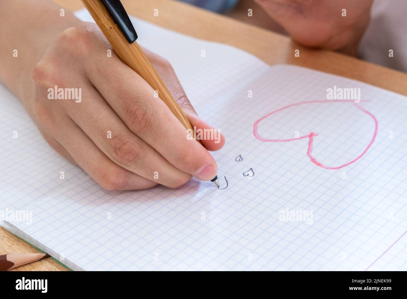 A child's hand drawing hearts in a notebook. A secret declaration of love. The child dreams of love. Stock Photo