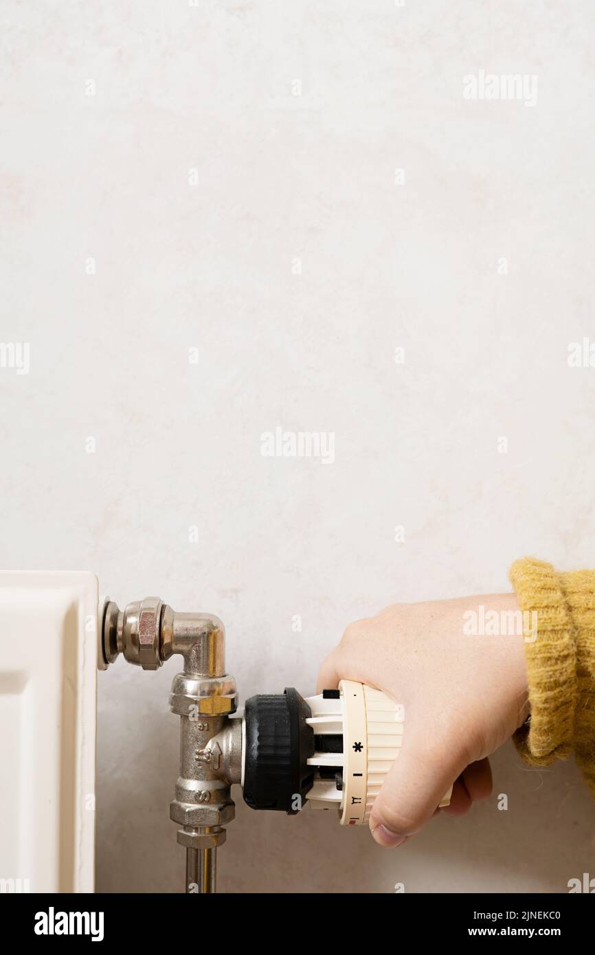 Person turning off the heating, radiator while wearing a warm yellow sweater. Concept of saving