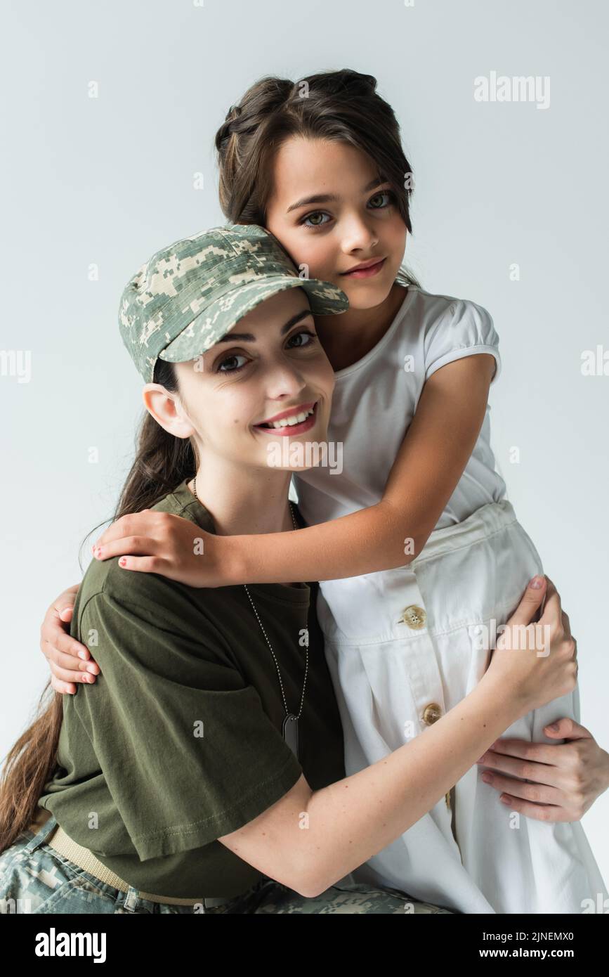 Smiling mother in military uniform looking at camera while hugging kid