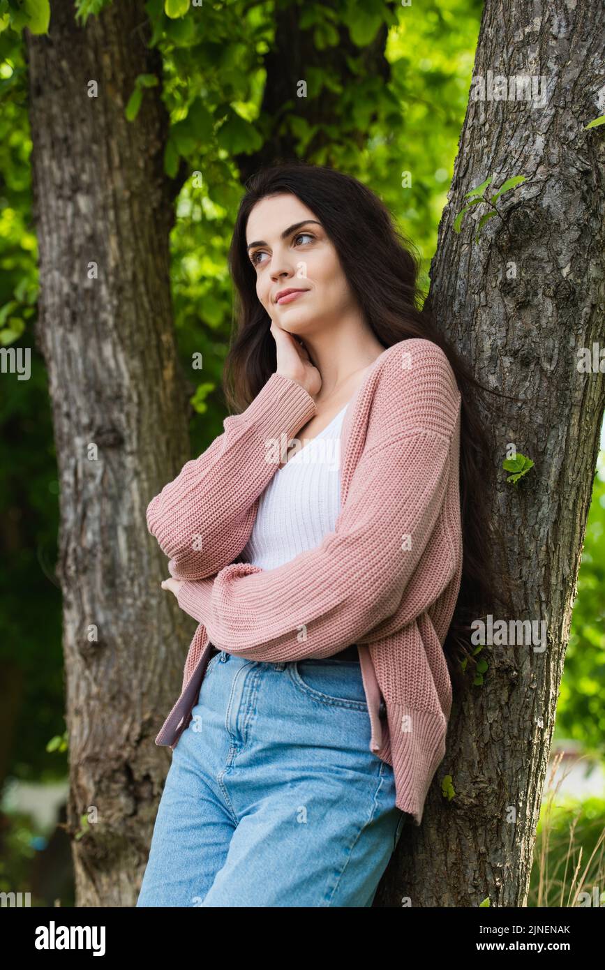 pensive brunette woman in knitted cardigan looking away in park,stock image Stock Photo