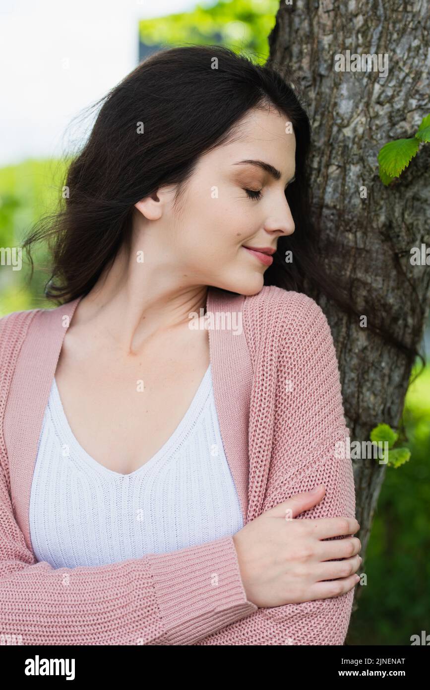 happy brunette woman with closed eyes standing near tree trunk,stock image Stock Photo