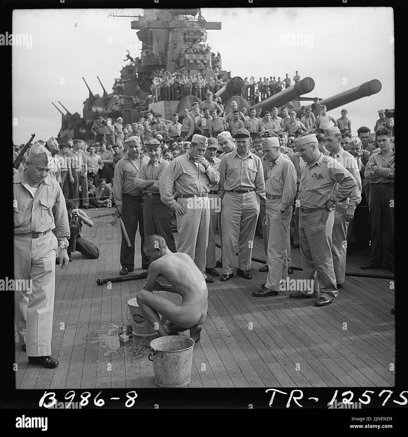 The crewmen of the battleship USS New Jersey watch a Japanese prisoner of war bathe himself before he is issued GI... Stock Photo