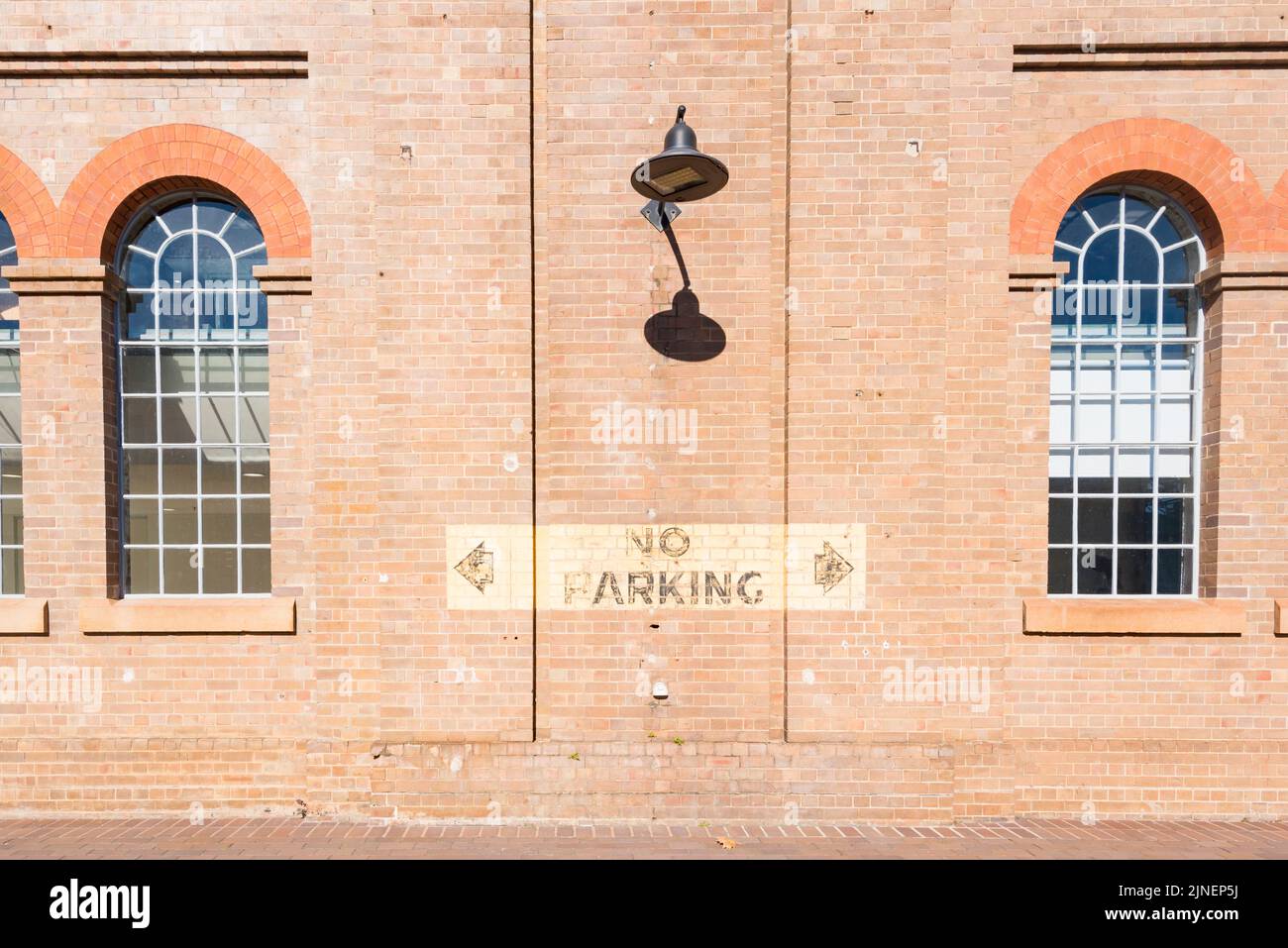 A tall brick wall with an antique style LED floodlight and a vintage No Parking sign at the National Innovation Centre in South Ev Stock Photo
