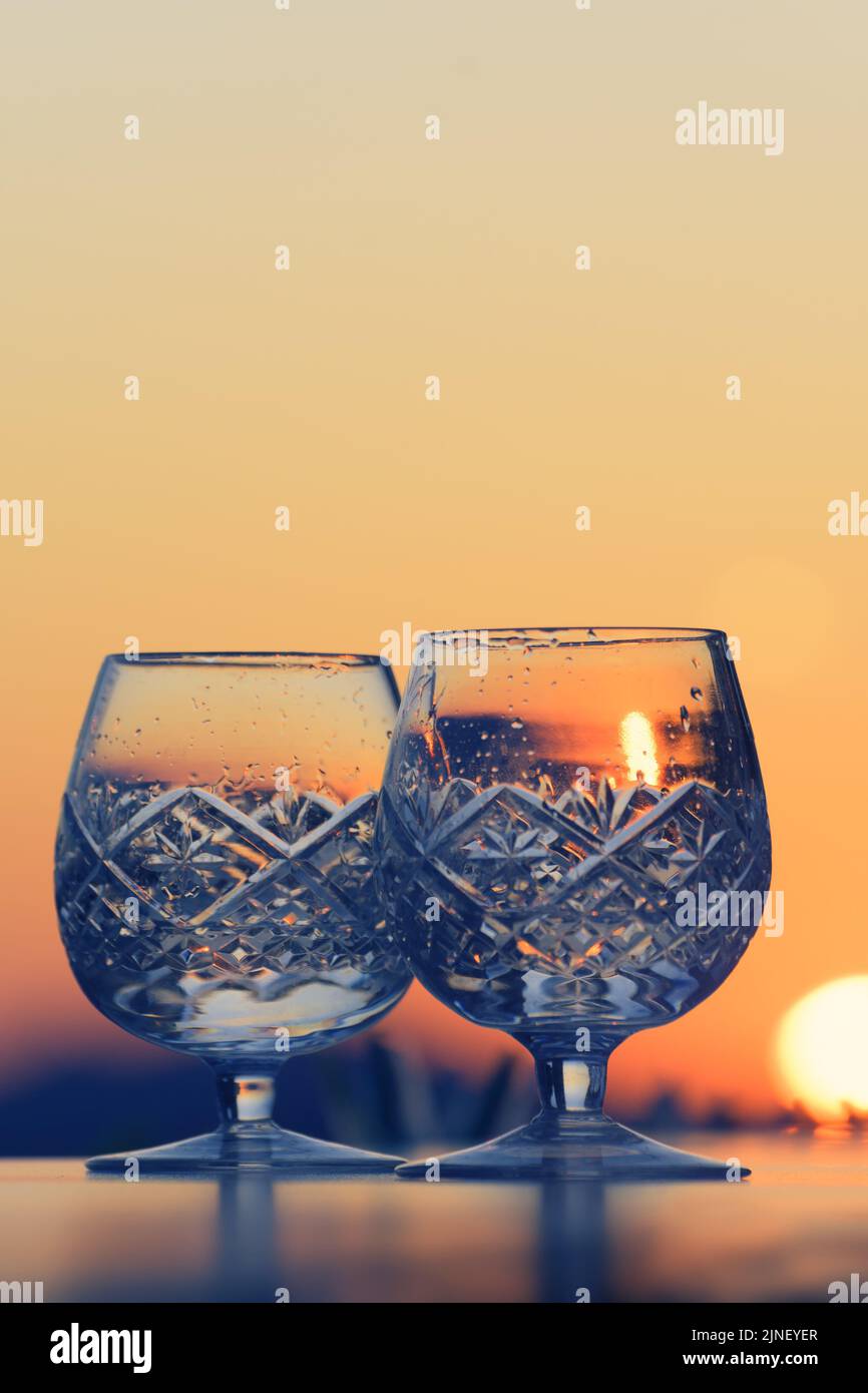 Romantic view of two crystal glasses with water droplets and sunset in background Stock Photo