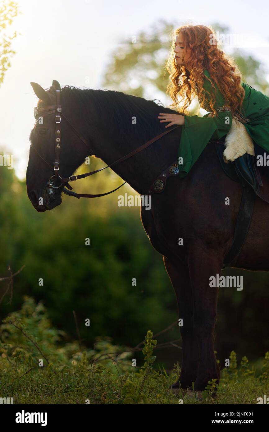 Medieval woman princess in green dress sits astride black steed horse. Girl  rider in vintage cloak cape train flies in wind motion. Background green t  Stock Photo - Alamy
