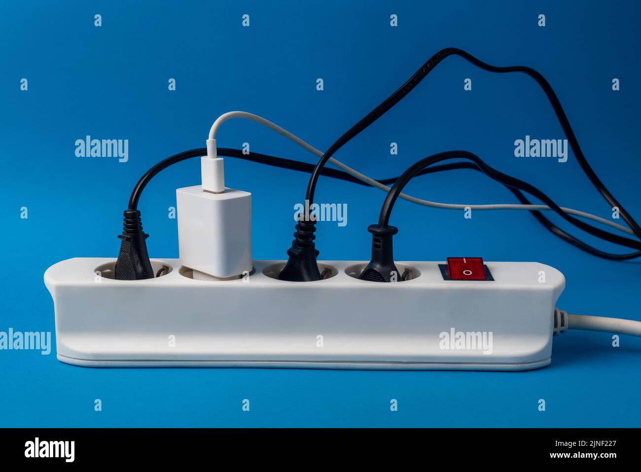 Multi-plug power strip with many connected devices on blue background. Concept of energy abuse. Waste and squandering of electricity Stock Photo