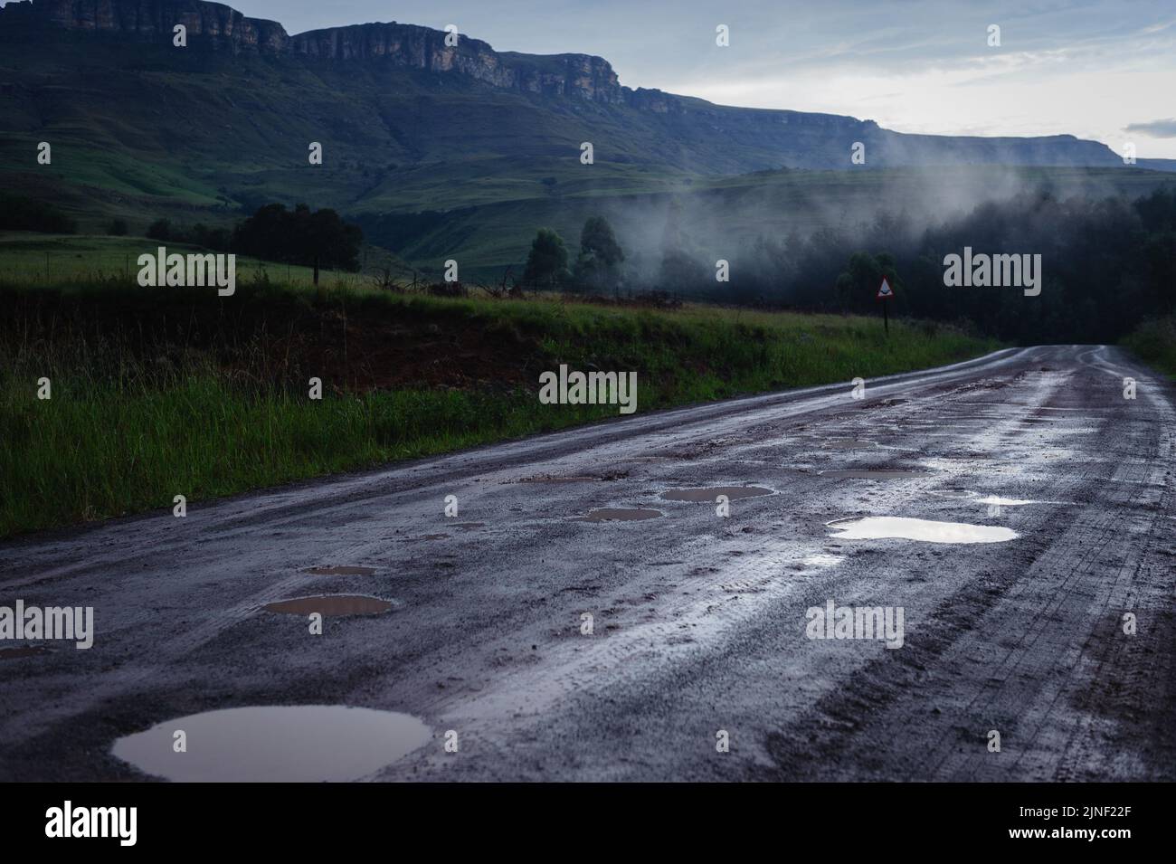 A road winding through South Africa's Kamberg Valley in the Drakensberg mountains after a winter rain Stock Photo