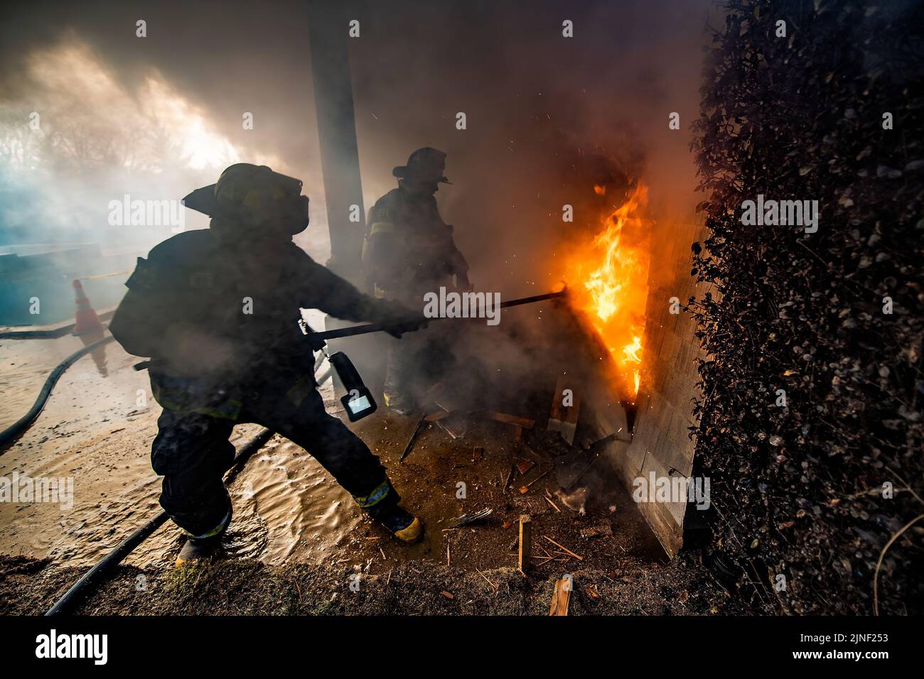 A firefighter uses a hook to remove siding from the house to expose the fire inside the walls as the Bridgehampton Fire Department, with mutual aid fr Stock Photo