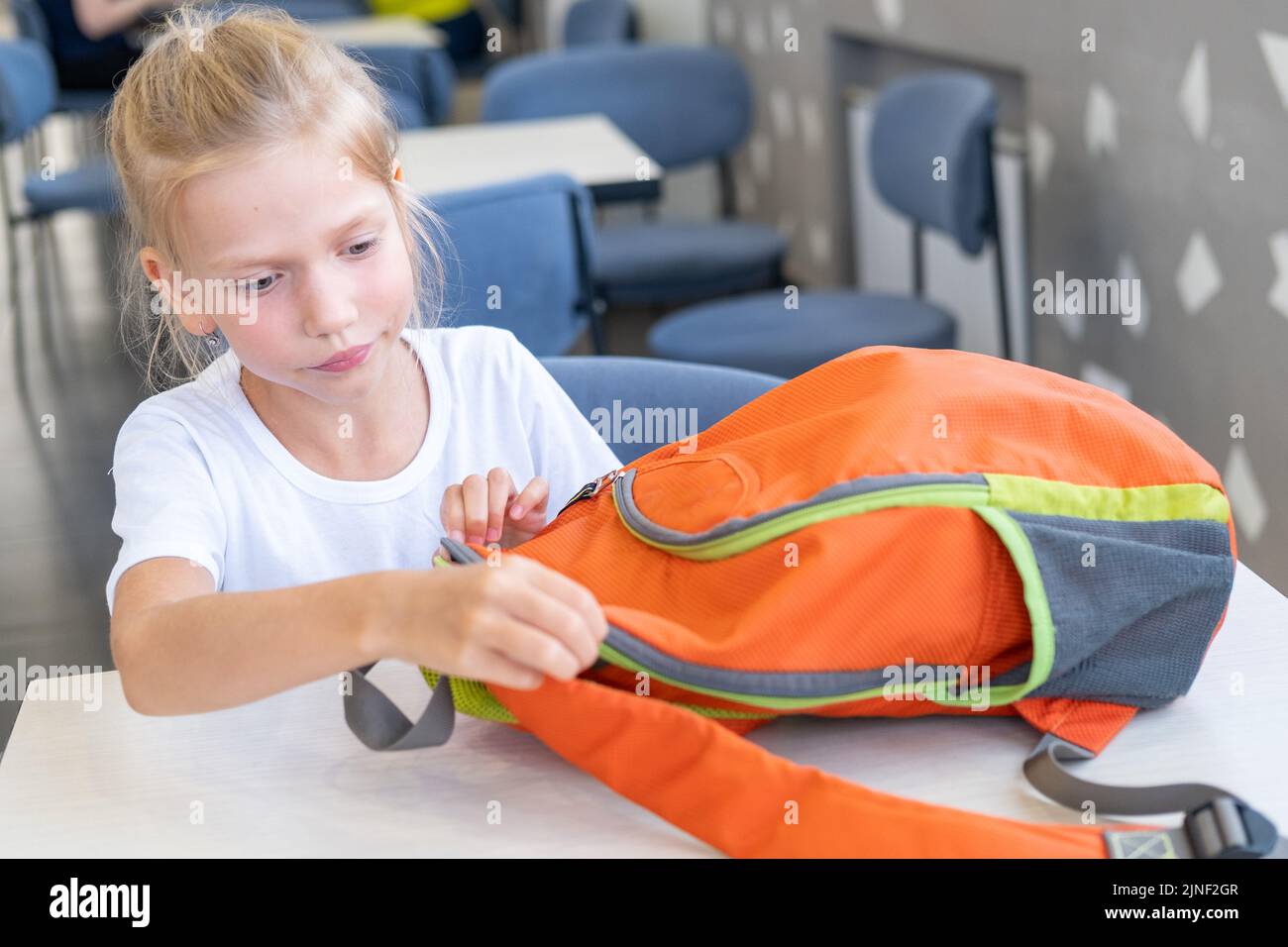 A student girl puts stationery in a backpack. A child zips up a school