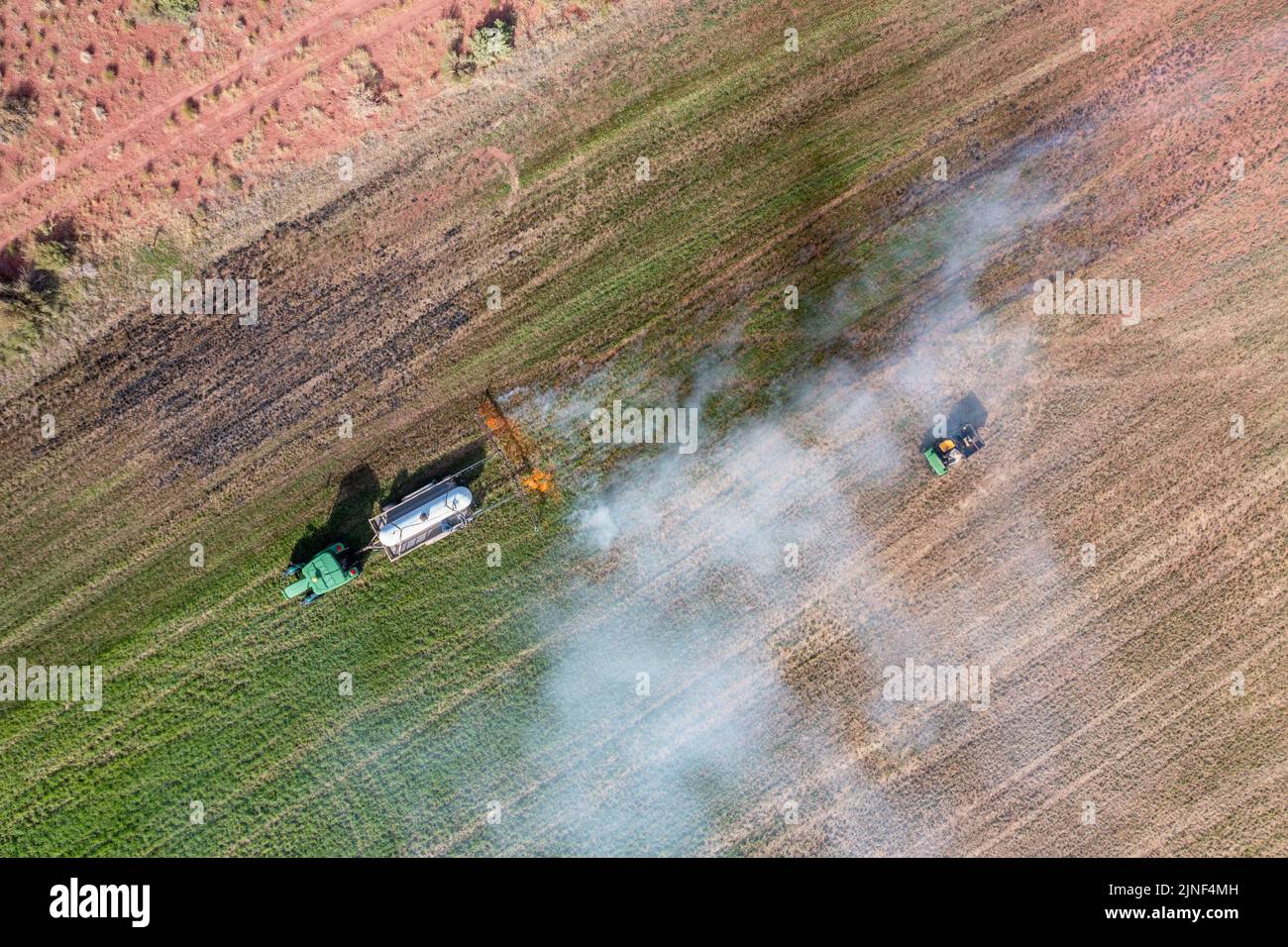 A tractor pulling a propane burner burns weeds in an hayfield after