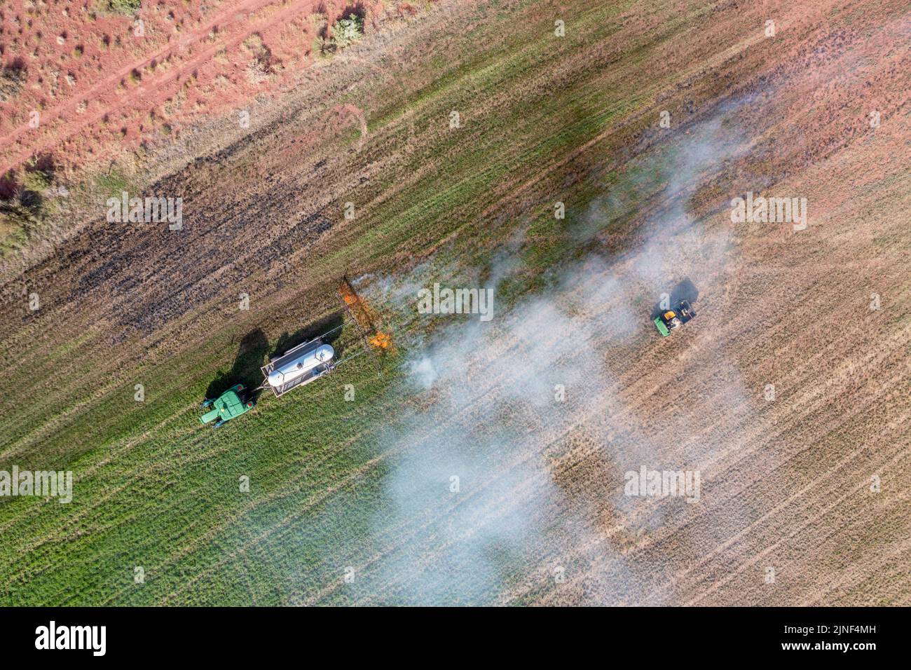 A tractor pulling a propane burner burns weeds in an hayfield after cutting the alfalfa on a ranch in Utah. Stock Photo