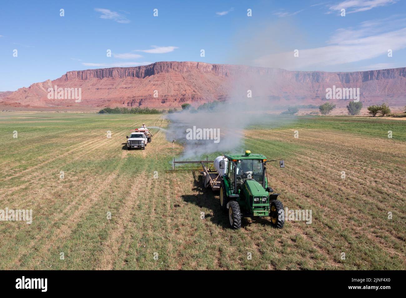 A tractor pulls a propane burner to burn weeds in an hay field after cutting the alfalfa on a ranch in Utah.  A water truck follows to control the fir Stock Photo