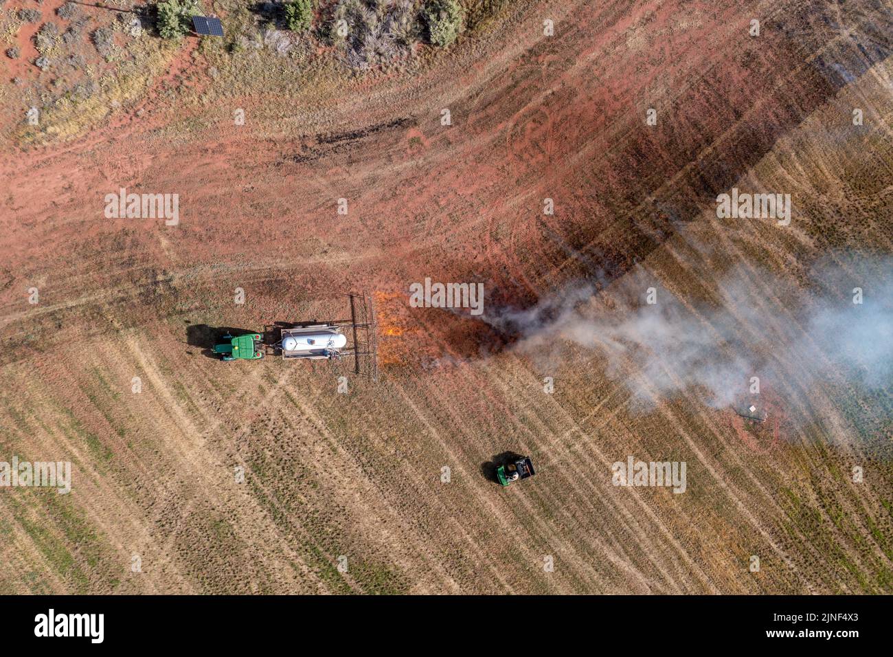 A tractor pulling a propane burner burns weeds in an hayfield after cutting the alfalfa on a ranch in Utah. Stock Photo