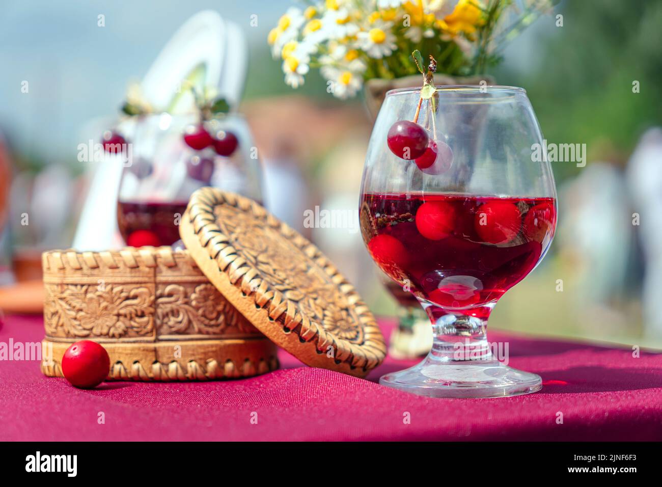sweet cherry tincture in a glass with berries on the table and a wooden box. Alcoholic National Beverage Stock Photo