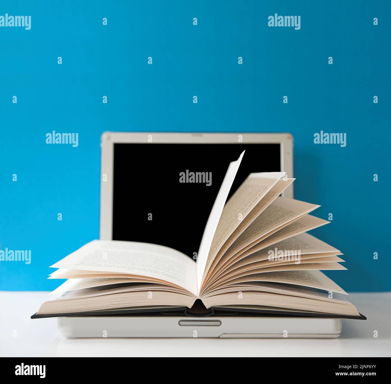 Open book on top of a laptop computer - focus on the tips of the page leaves. Stock Photo