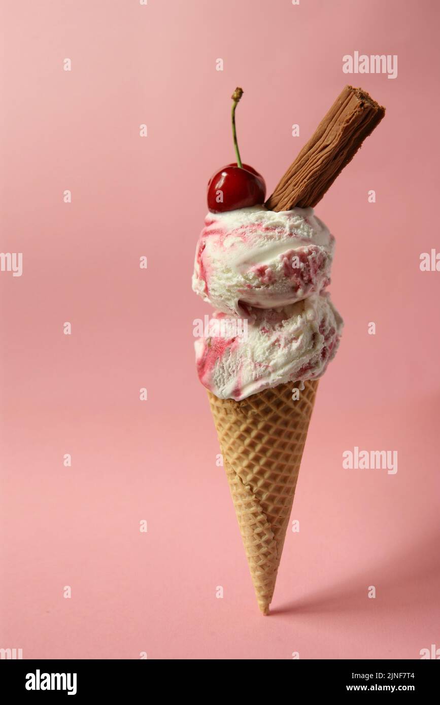 Ice cream cornet with raspberry/strawberry flavour - garnished with a cherry and chocolate against a pink background Stock Photo