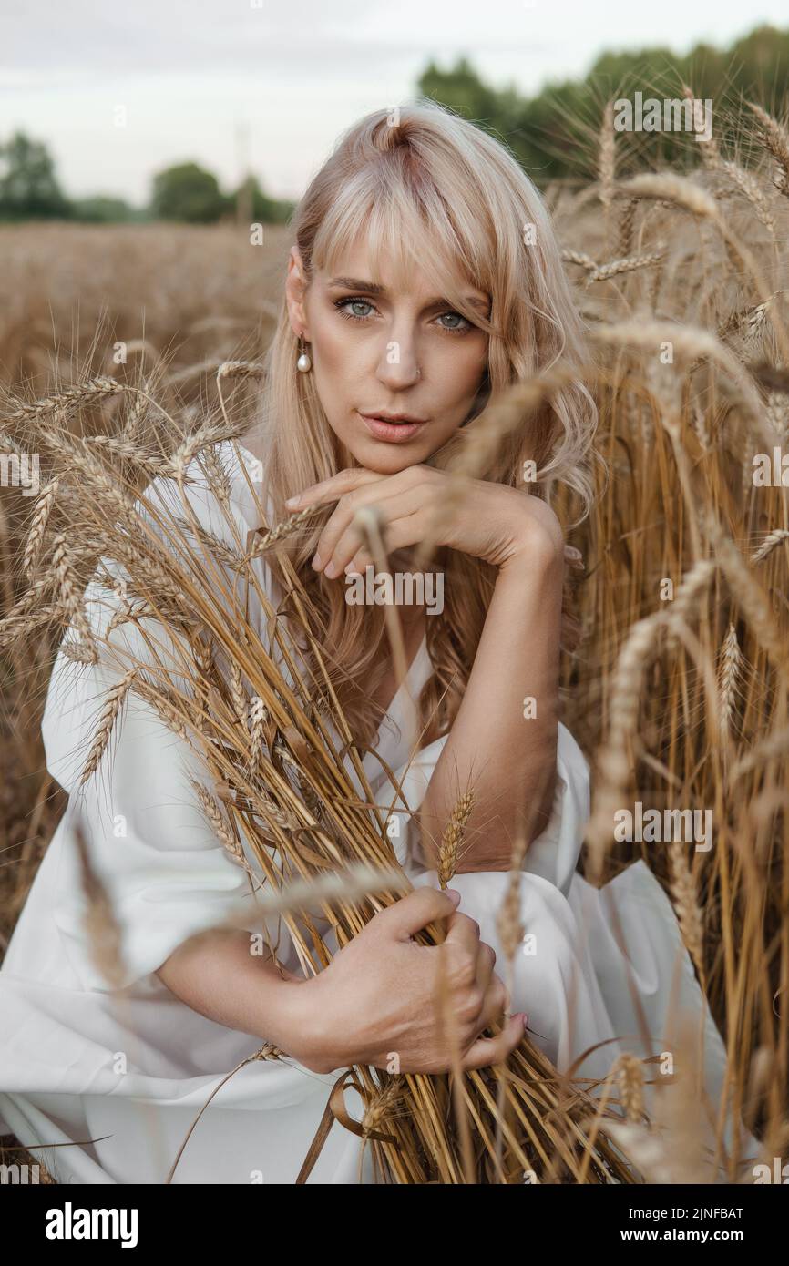 A blonde woman in a long white dress walks in a wheat field. The ...