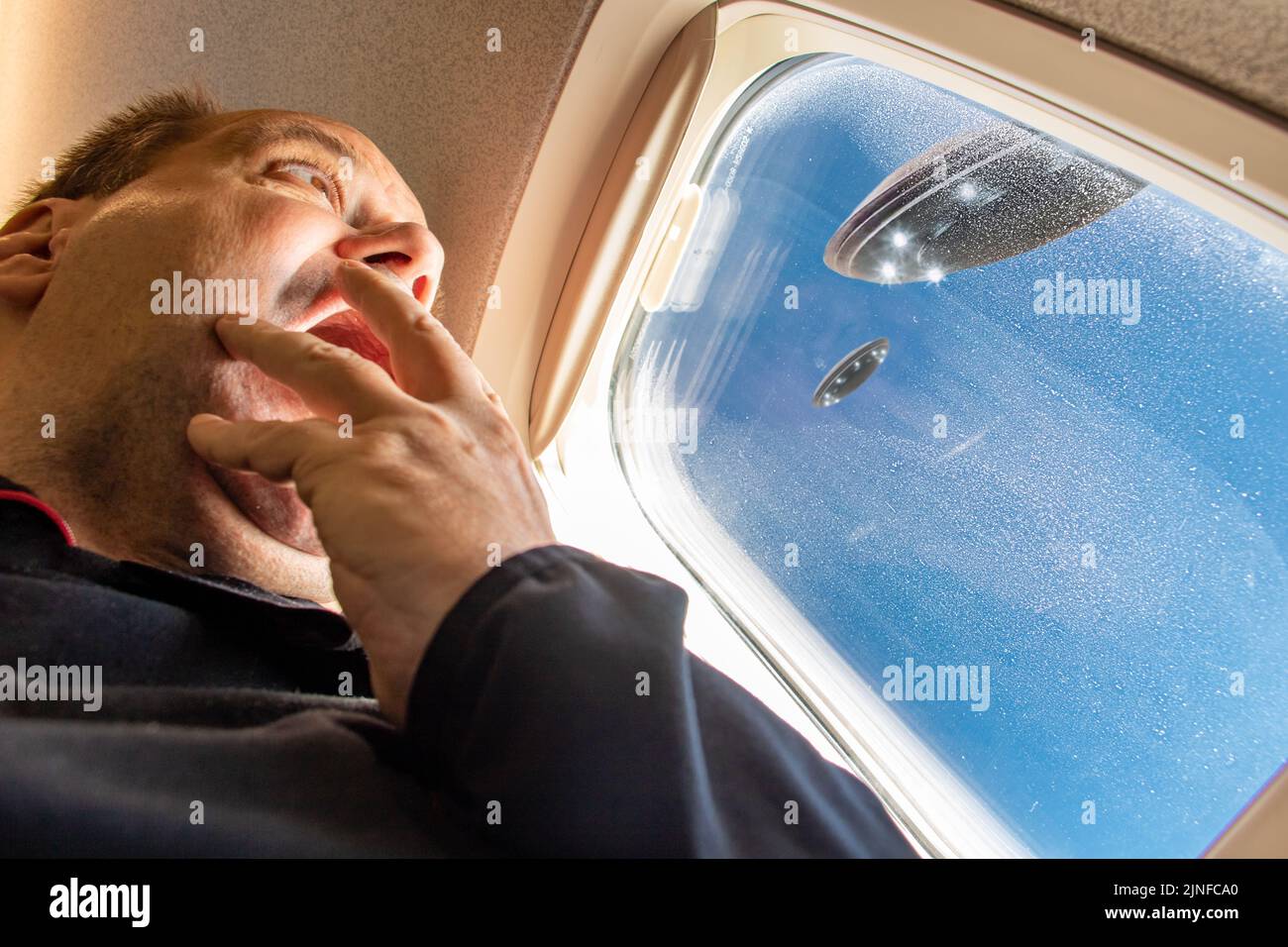 A frightened man looks at a UFO from the window of a flying plane Stock Photo