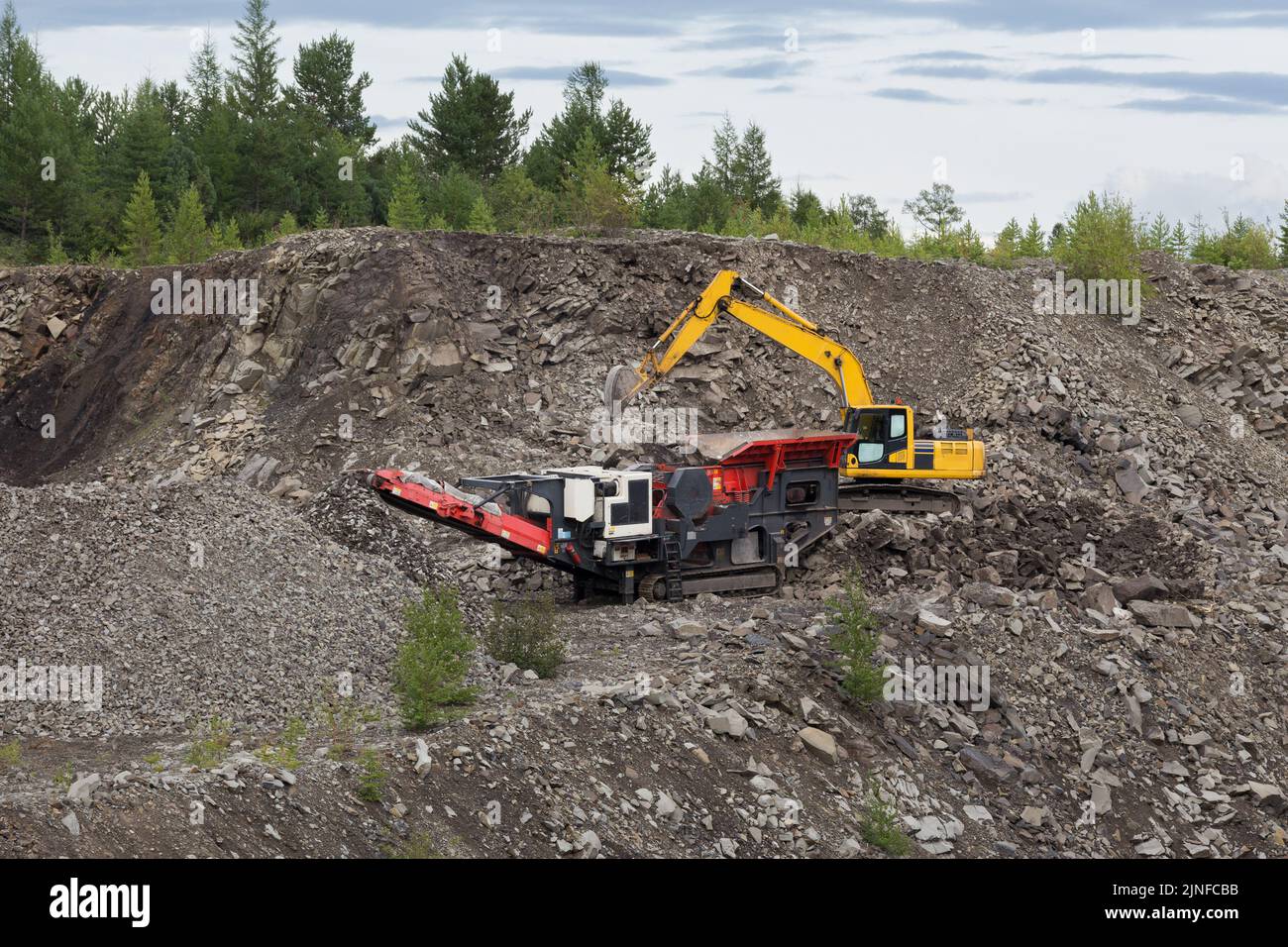 An excavator and a crusher extract crushed stone in a quarry. Stock Photo