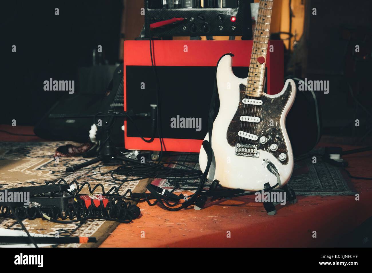 A white electric guitar and a red amplifier onstage with electrical