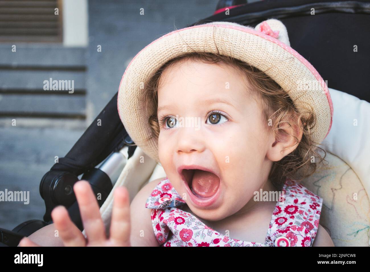 A cute white Caucasian little girl wearing a round straw summer hat looking surprised and happy Stock Photo
